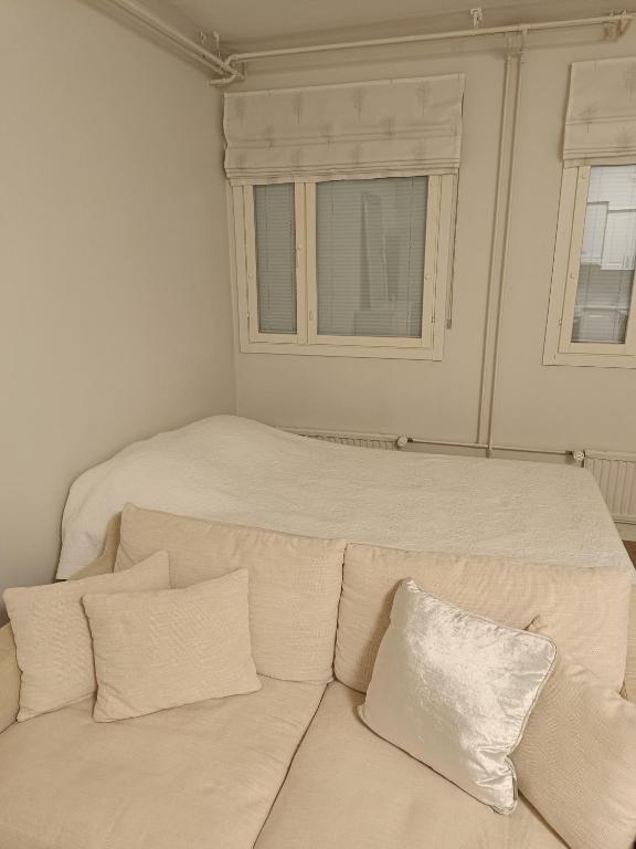 Vaalean beige sohva, jossa on tyynyjä, valkoisen peiton alla ikkunoiden edessä.